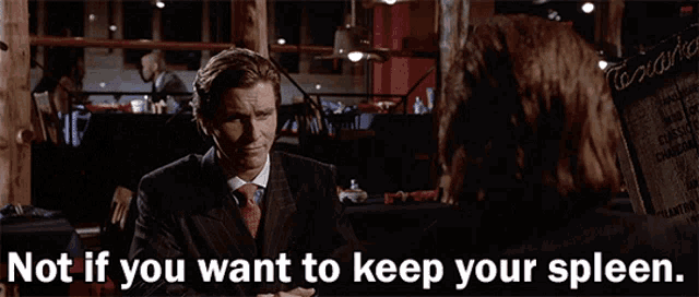 a man in a suit and tie talking to another man with the words not if you want to keep your spleen