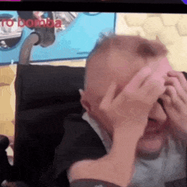 a man in a wheelchair is covering his face with his hands in front of a tv screen that says to bomba