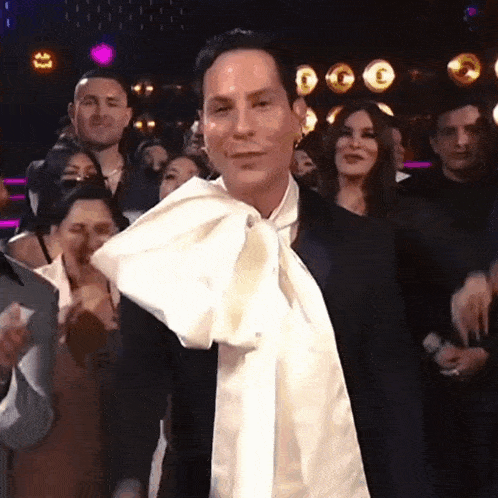 a man in a tuxedo with a white scarf around his neck is standing in front of a crowd of people