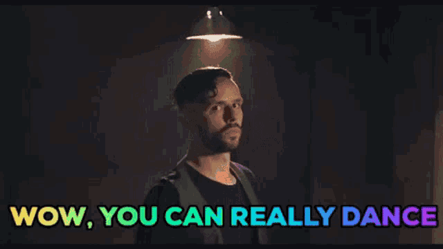 a man with a beard is standing in a dark room and says wow you can really dance .
