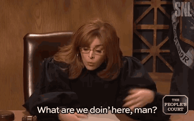 a woman in a judge 's robe is sitting at a desk and says what are we doin ' here man