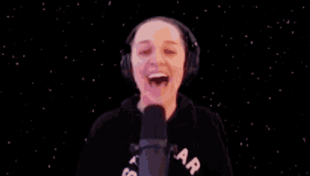 a woman wearing headphones is laughing in front of a microphone in a dark room .