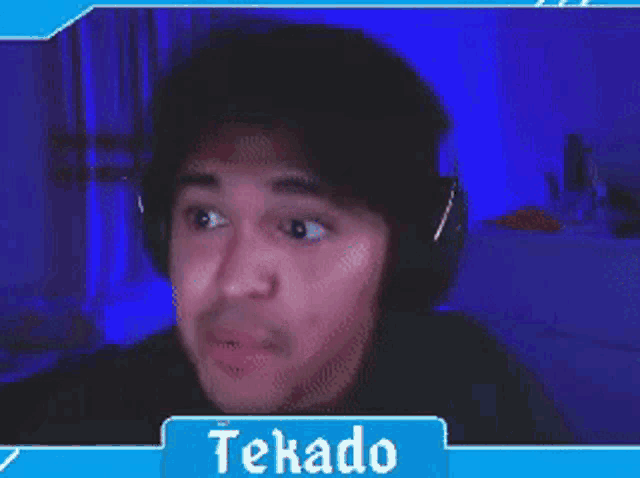 a man wearing headphones is making a funny face in front of a blue screen that says tekado