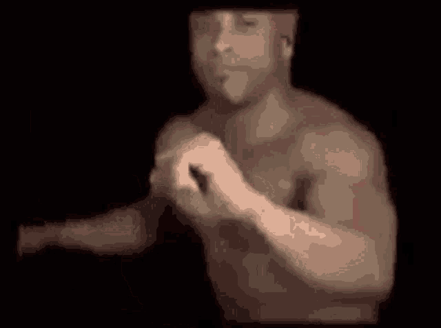 a shirtless man with a red bandana on his head is dancing in a dark room .