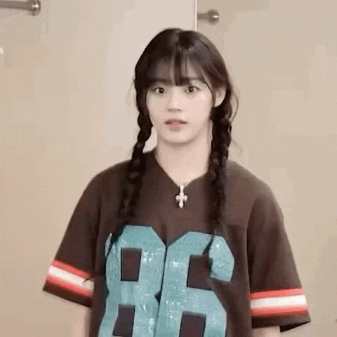 a girl with braids is wearing a brown t-shirt with the number 86 on it and a cross necklace .