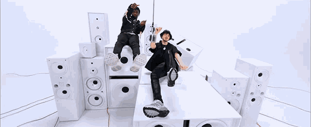 a couple of people sitting on top of a stack of white speakers