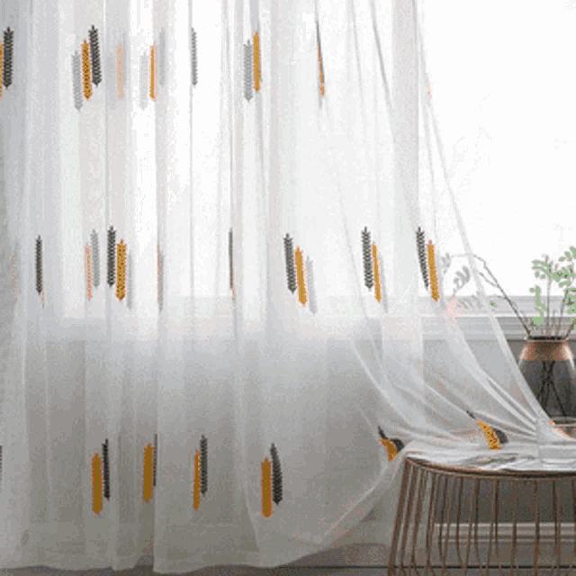 a white curtain with yellow and gray embroidery hangs over a window
