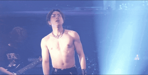 a shirtless man stands on a stage in front of a guitar player