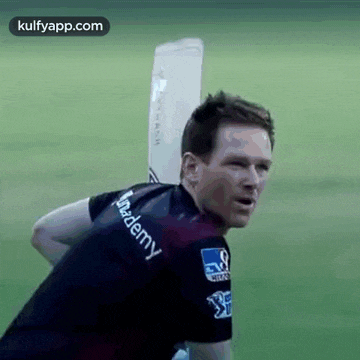 a man in a black shirt is holding a cricket bat on his shoulder .