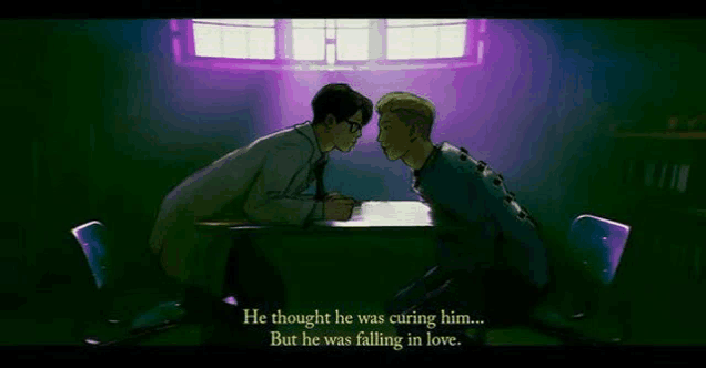 a man is sitting at a table with another man and they are looking at each other in a dark room .