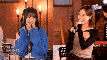 two girls are singing into microphones and one of them is wearing a blue sweater .