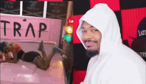 a man in a white hoodie is standing in front of a picture of a woman laying on a bed .