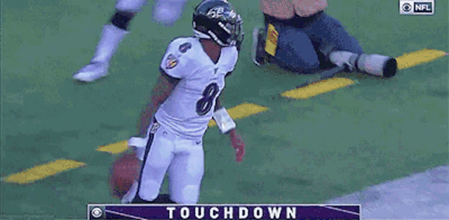 a football player in a ravens uniform is holding a ball in front of a touchdown screen