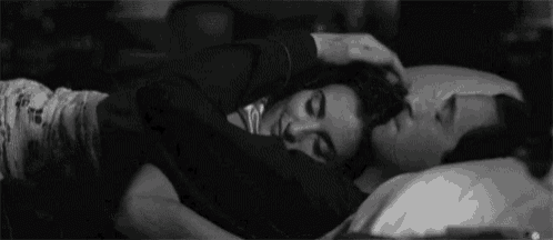 a black and white photo of a man and woman hugging each other while sleeping on a bed .