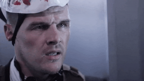 a man wearing a helmet with blood on it and a bandage on his head .
