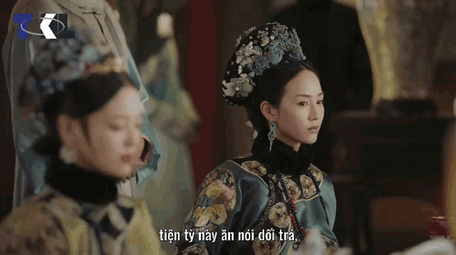 a woman with a crown on her head stands next to another woman in a green dress