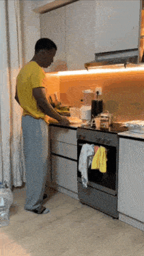 a man in a yellow shirt stands in a kitchen preparing food