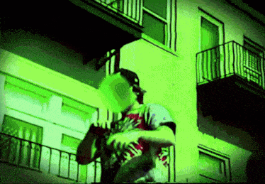 a man standing on a balcony with a green light behind him and a shirt that says ' ain '