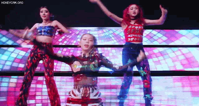 three women are dancing on a stage with a disco ball in the background .