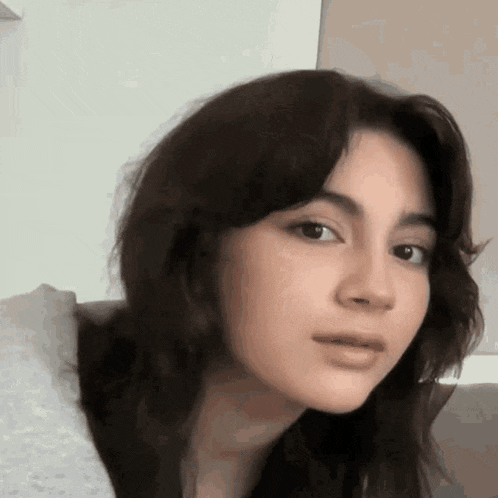 a young woman with long dark hair is sitting on a couch and making a funny face .