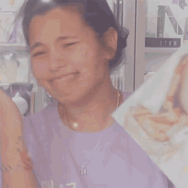 a woman in a purple shirt is smiling in front of a shelf with figurines on it