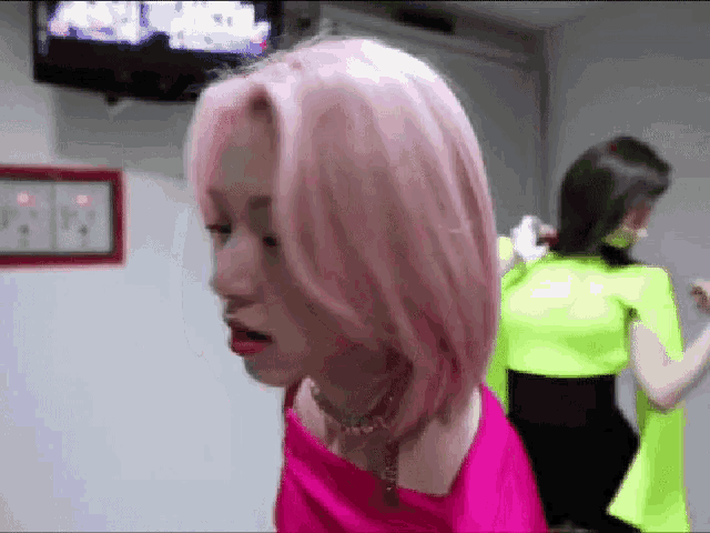a woman with pink hair is standing next to another woman in a neon green top .
