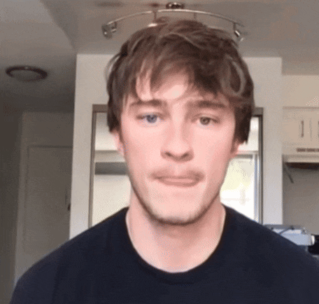 a young man with a beard is making a funny face while wearing a black t-shirt .