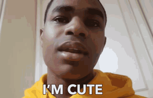 a young man wearing a yellow hoodie has the words i 'm cute written on his face