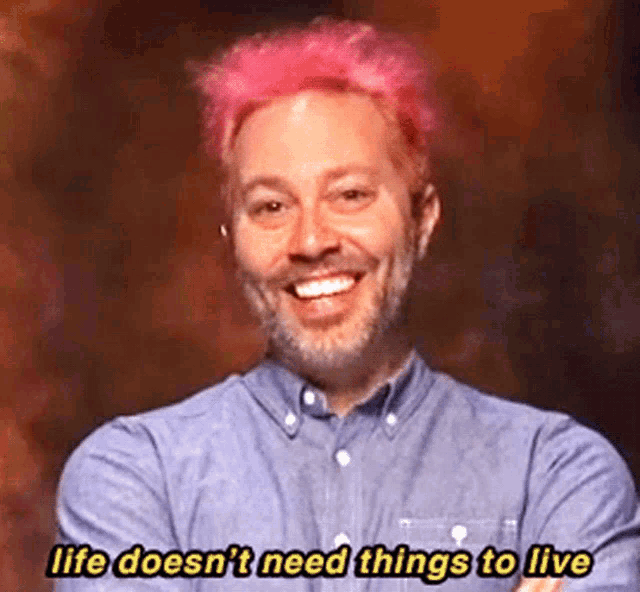 a man with pink hair and a beard is smiling and says life does n't need things to live