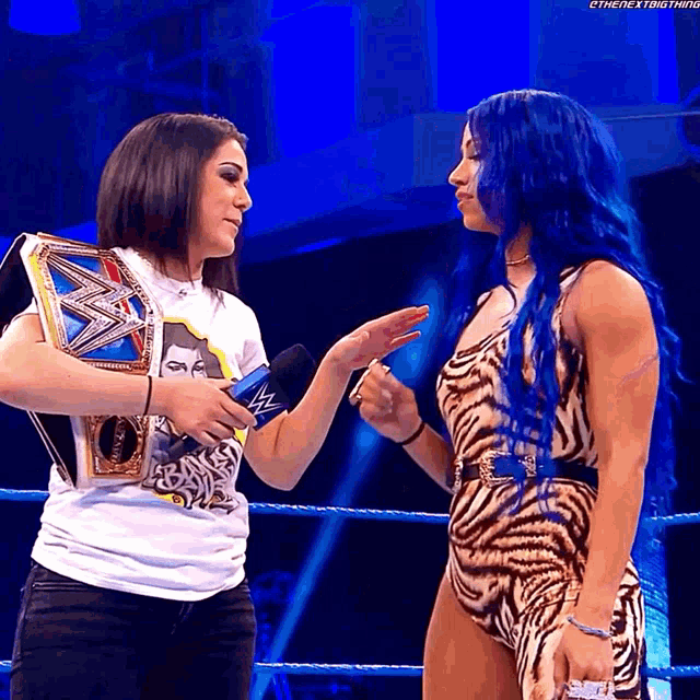 a female wrestler with blue hair is talking to another woman in a wrestling ring