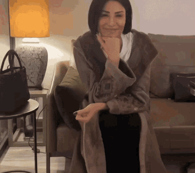 a woman in a fur coat sits on a couch in front of a lamp