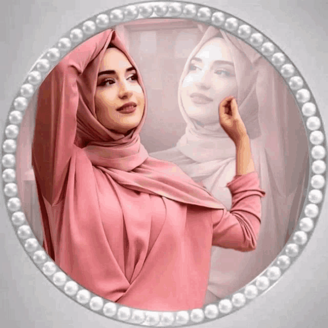 a woman in a pink hijab stands in front of a mirror with pearls around it
