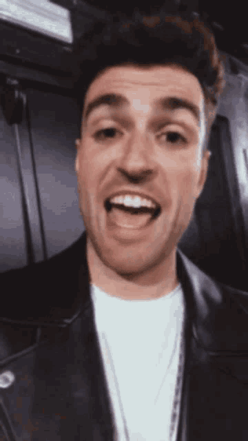a man wearing a white shirt and a leather jacket is smiling