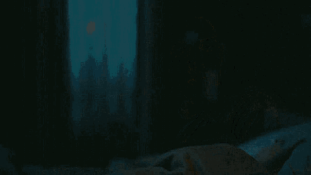 a man in a gray shirt is sitting in a dark room .