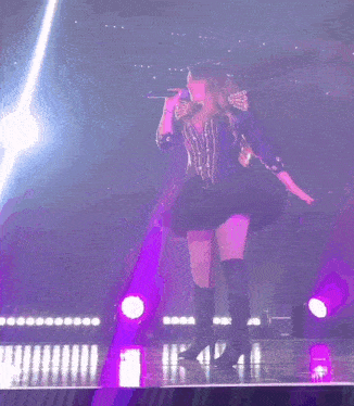 a woman singing into a microphone on a stage with purple lights behind her