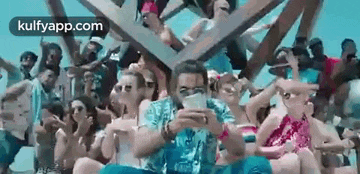 a man is sitting in front of a crowd of people on a beach looking at his phone .