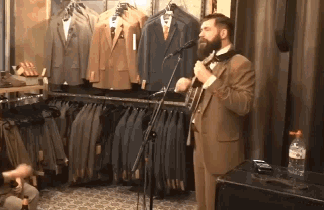 a man in a suit singing into a microphone in front of a rack of suits