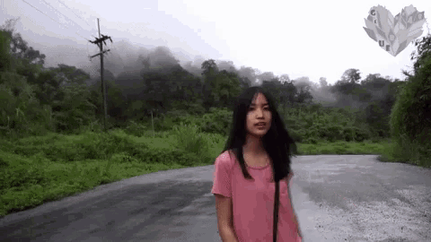 a woman in a pink shirt is walking down a road surrounded by trees