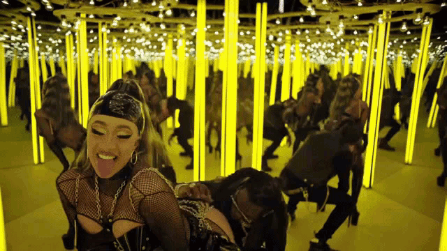 a woman is sticking her tongue out while dancing in a mirrored room filled with yellow lights .