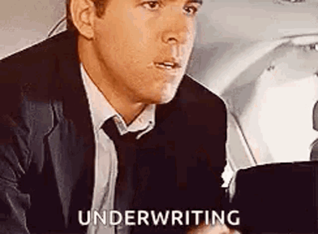 a man in a suit and tie is sitting in the back seat of an airplane and saying `` underwriting '' .