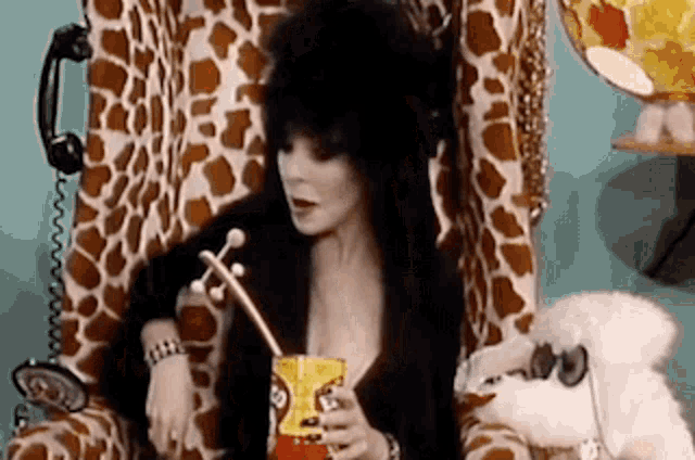 a woman is sitting in a giraffe chair holding a drink through a straw and eating chips .