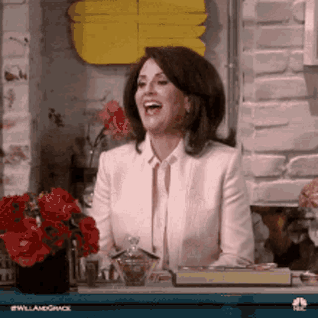 a woman in a pink suit is laughing in front of a brick wall