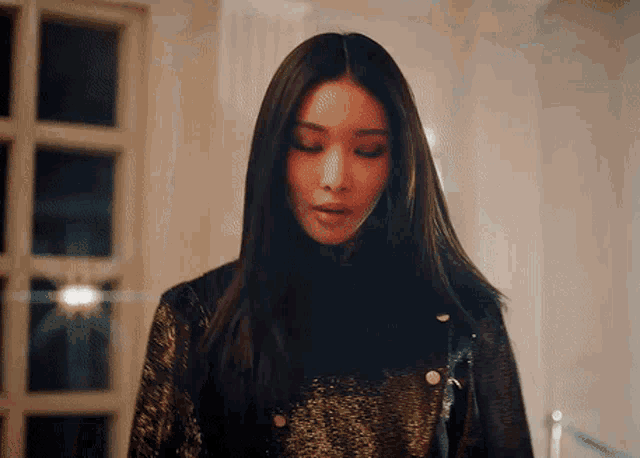 a woman with long black hair is wearing a black and gold jacket .
