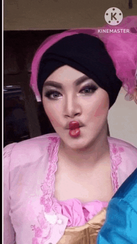 a woman wearing a pink dress and a black turban is making a funny face with her lips .