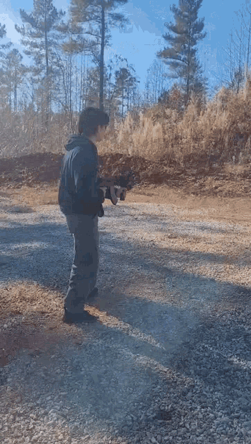 a man is holding a gun in a gravel area