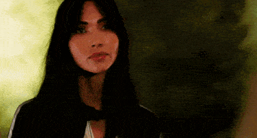 a woman with long black hair is looking at the camera with a serious expression on her face .