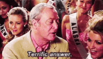 a man in a suit is talking to a group of women while wearing an alaska sash .