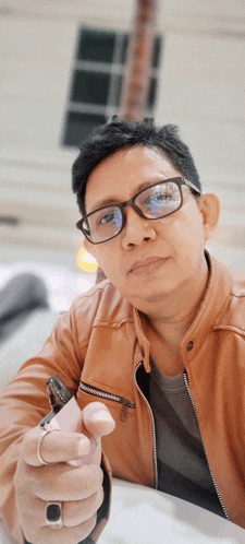 a man wearing glasses and a brown jacket is holding a lighter in his hand