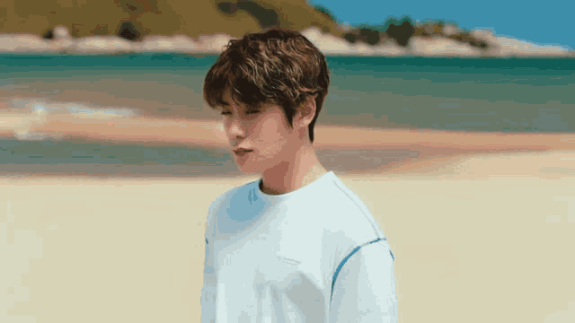 a young man in a white shirt is standing on a beach near the water