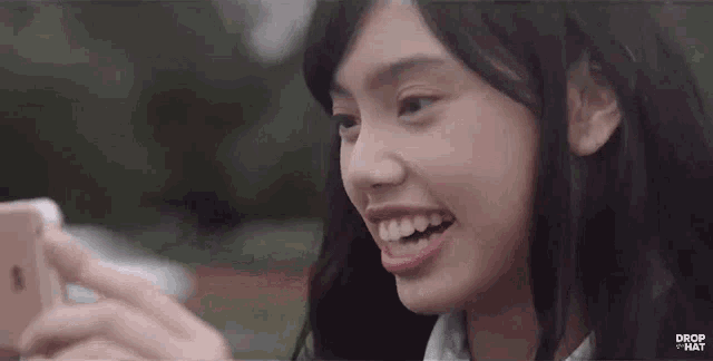 a girl is smiling while looking at her phone and the word drop that is on the bottom of the screen